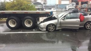 Silver sedan wedged under a flatbed trailer after a rear-end crash