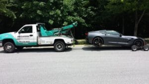 Tow truck lifting a damaged dark sedan with its wheel lift
